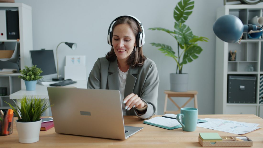 A woman using a headset and laptop in a home office.