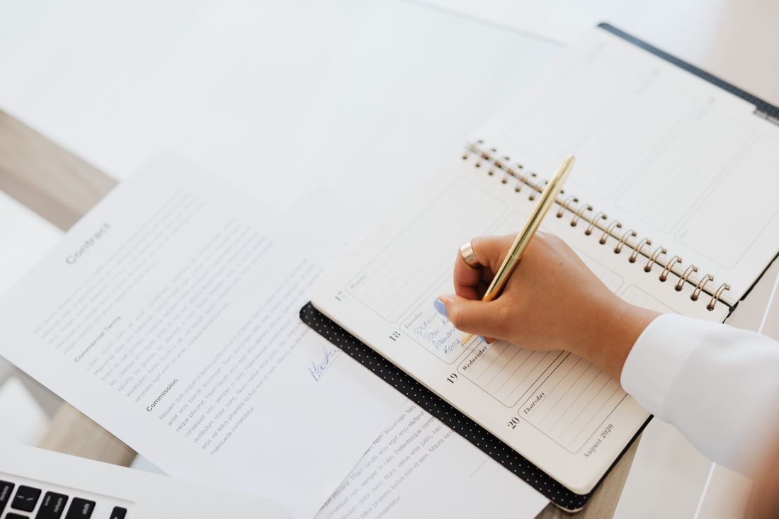 A person writing notes in a planner beside paperwork.